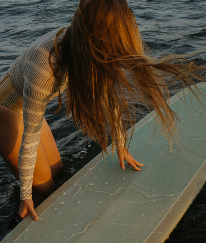 Woman with long hair in the water holding a surfboard, capturing a moment of instant karma on the ocean surface.