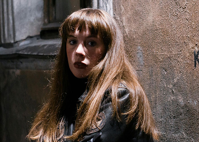 Young woman with long brown hair and leather jacket in a dimly lit alley, evoking bizarre events that creep people out.