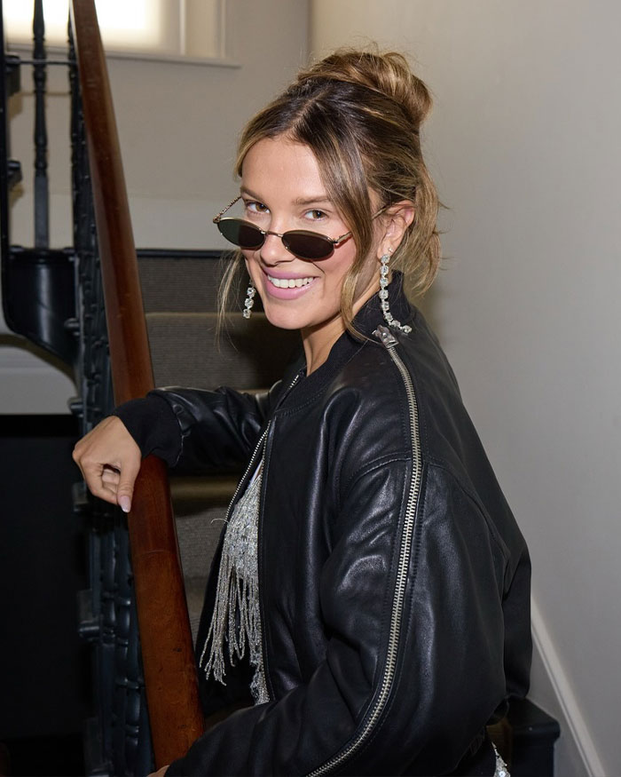 Millie Bobby Brown smiling in sunglasses and leather jacket, fans furious over legally changing her name news.