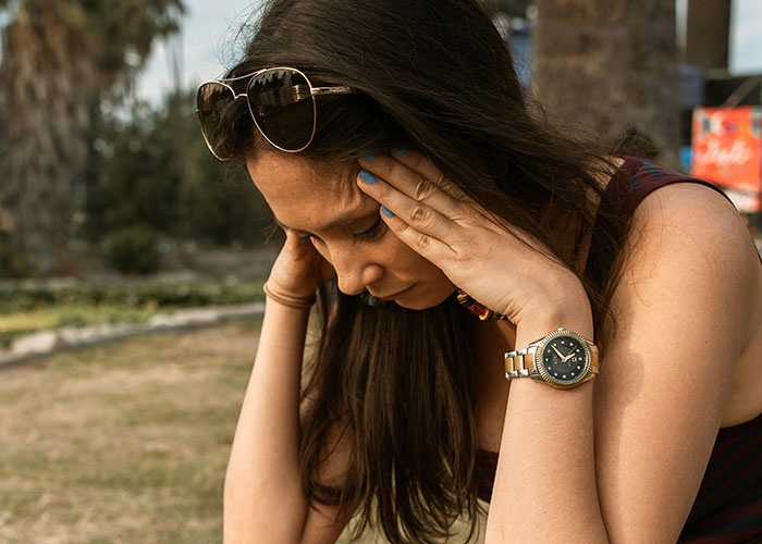 Young woman outdoors looking stressed, holding her head, illustrating common challenges without life hacks shared by people.
