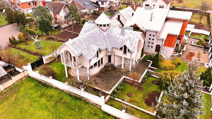Aerial view of a unique residential property surrounded by a white fence, part of wild real estate listings.