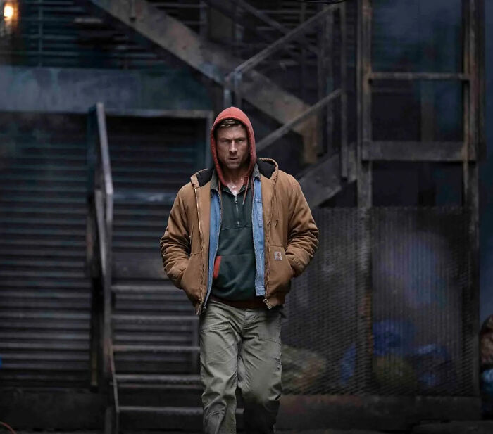 Man in layered jacket walking in dark urban setting, representing Hollywood's viral blunder and dark side exposure.