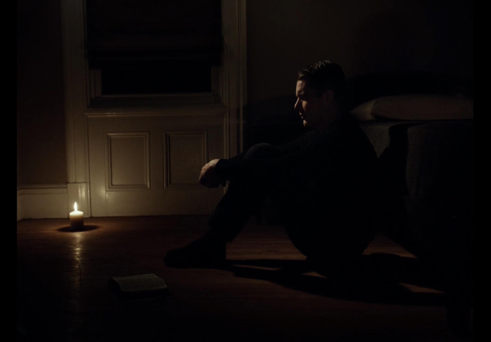 Person sitting on the floor in a dark room lit by candlelight, creating a spooky atmosphere for scary games with friends.