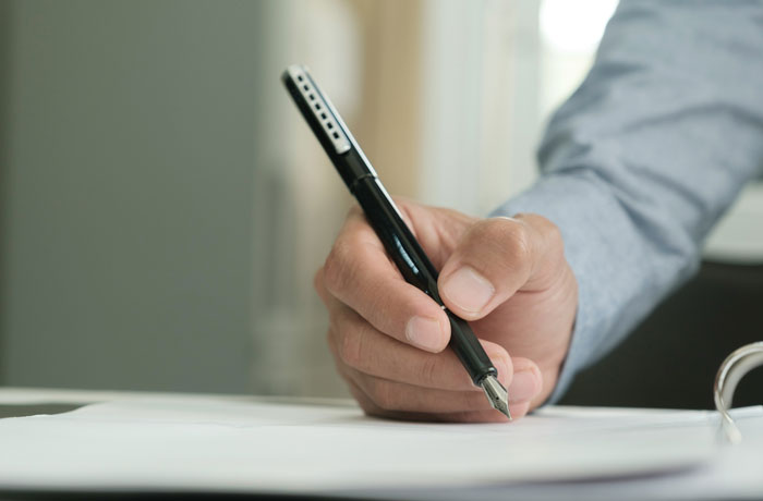 Person holding a pen and writing on paper, illustrating frustration with HOA rules and regulations.