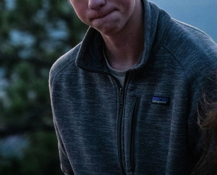 Young man wearing a grey Patagonia jacket with a tense expression, captured in an outdoor setting at dusk.