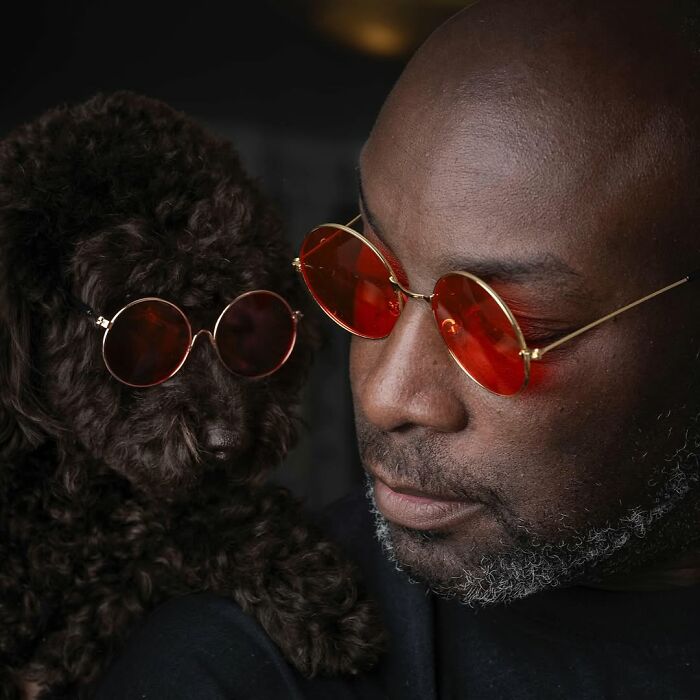 Man and his curly-haired dog wearing matching red sunglasses, showcasing pets and their humans who look alike.