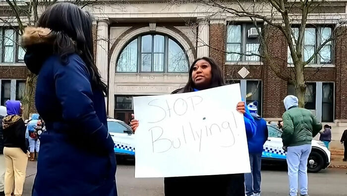 Woman holding stop bullying sign outside school after pregnant woman attacked by mob of young school kids