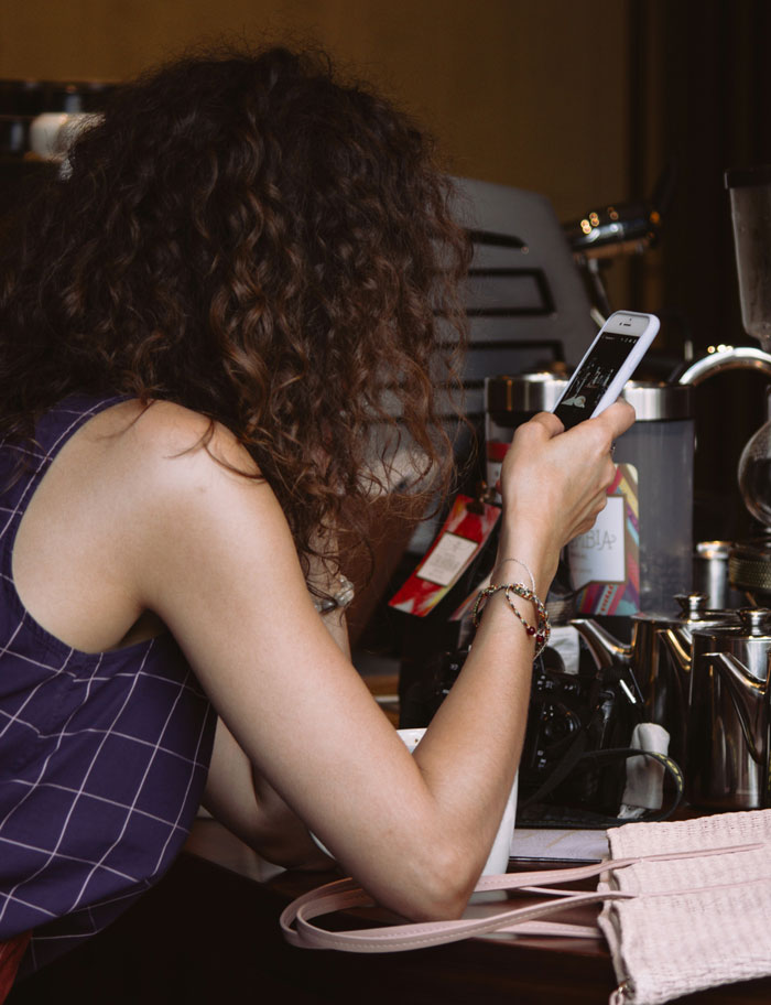 Woman with curly hair using smartphone at a cafe, illustrating communication and women girl code rules concept.