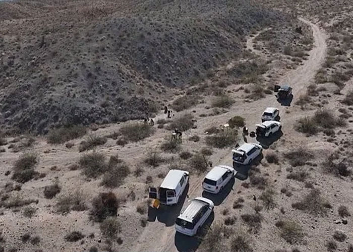 Aerial view of multiple white vans and people gathered on a dirt road in a desert area near Las Vegas museum.