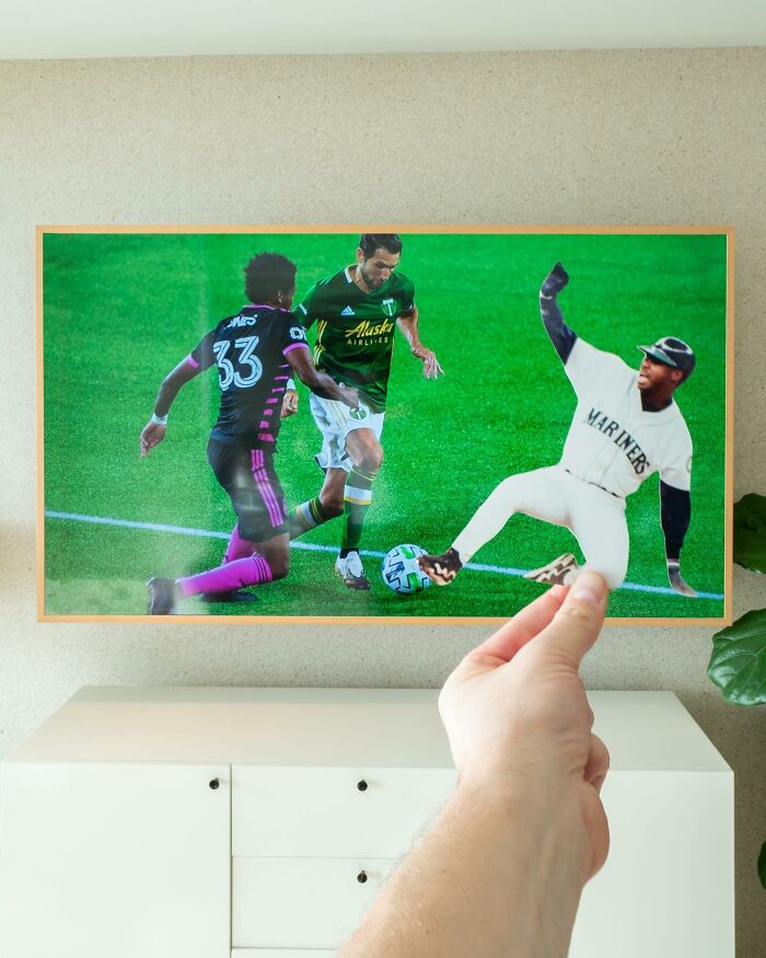 Hand holding paper cutout of baseball player interacting with soccer players on a framed photo, brilliant paper cutouts by Rudy Willingham.