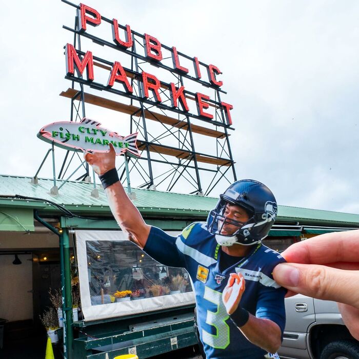 Hand holding paper cutout of football player interacting with Public Market sign in a street scene.