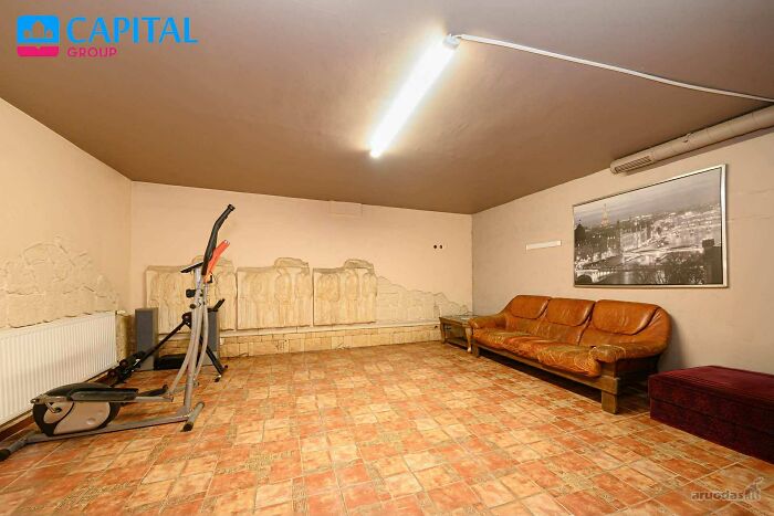 Basement room with worn leather couch, exercise equipment, tiled floor, and partially damaged wall in wild real estate listing.