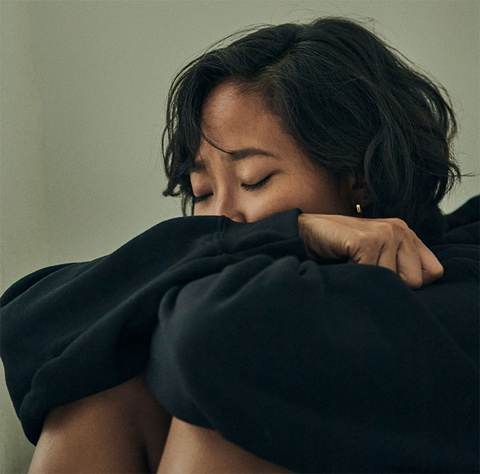 Woman in black hoodie sitting with eyes closed, upset after dress-code betrayal at Friendsgiving event. Woman in black hoodie sitting with eyes closed, upset after dress-code betrayal at Friendsgiving event.