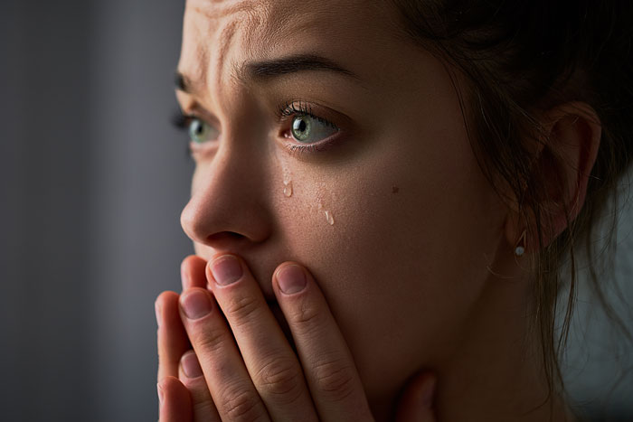 Close-up of a woman with tears on her face and hands covering her mouth, reflecting emotions tied to girl code rules.