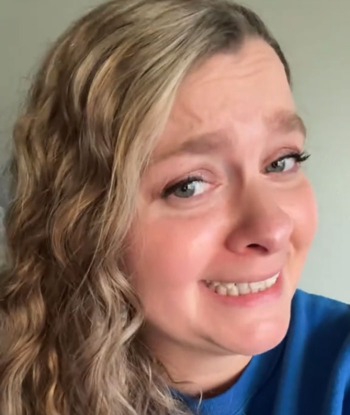 Close-up of a woman with wavy hair showing a strained smile, related to author calls women who read romantasy books.
