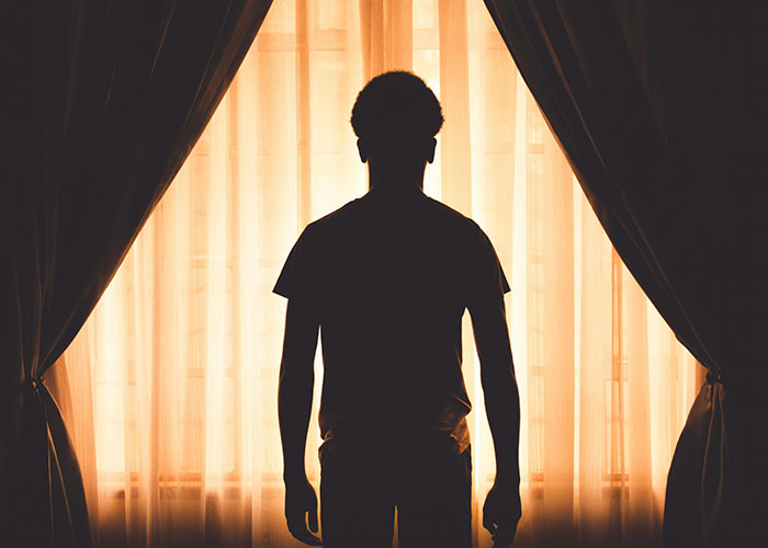 Silhouette of a person standing by a window with curtains, evoking a sense of bizarre events that creep people out.