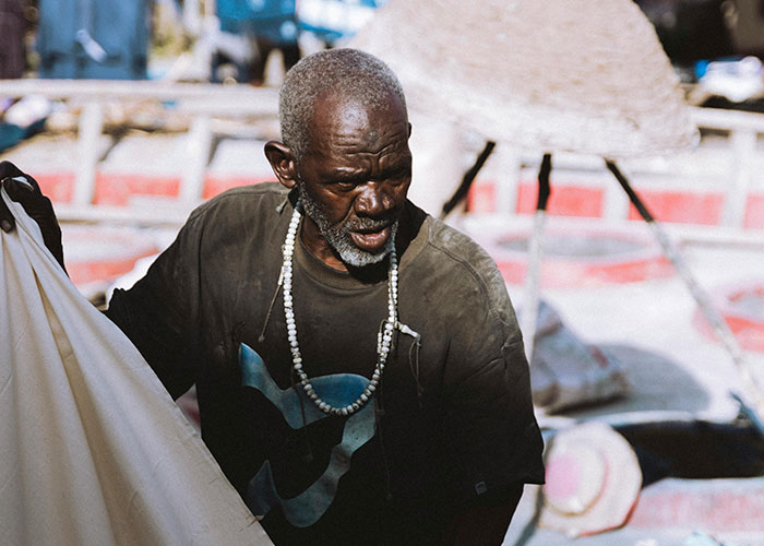 Elderly man in worn clothes working outdoors, highlighting harsh conditions in some of the worst cities worldwide to visit.