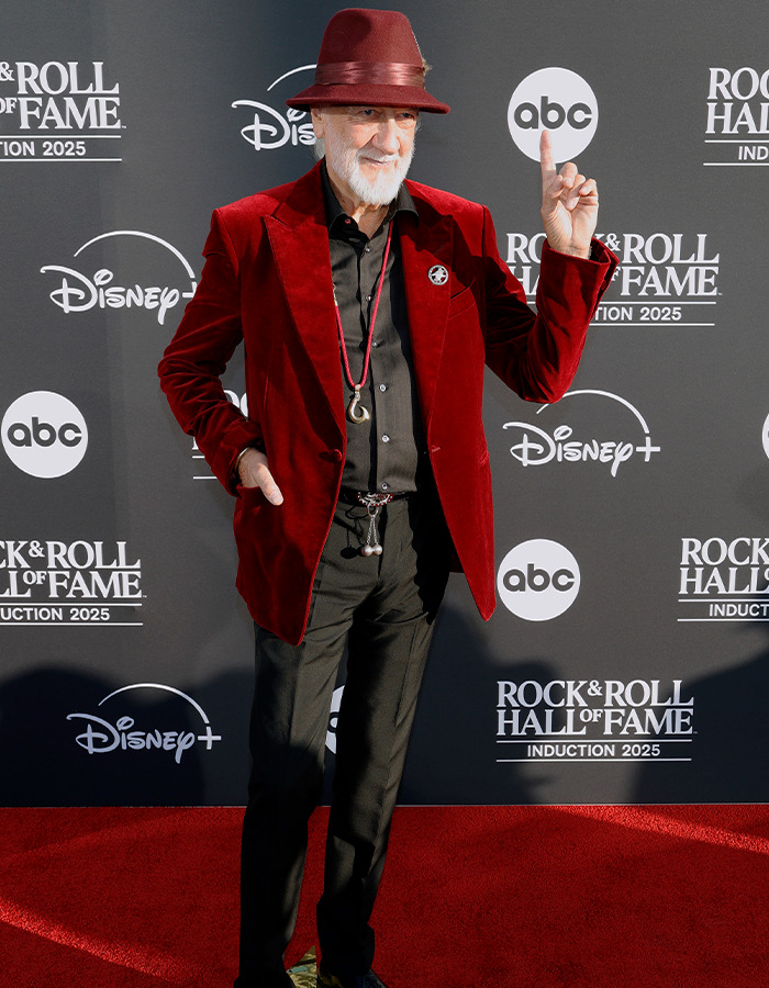 Man in red velvet blazer and hat posing on the red carpet at the Rock Hall of Fame 2025 fashion event.