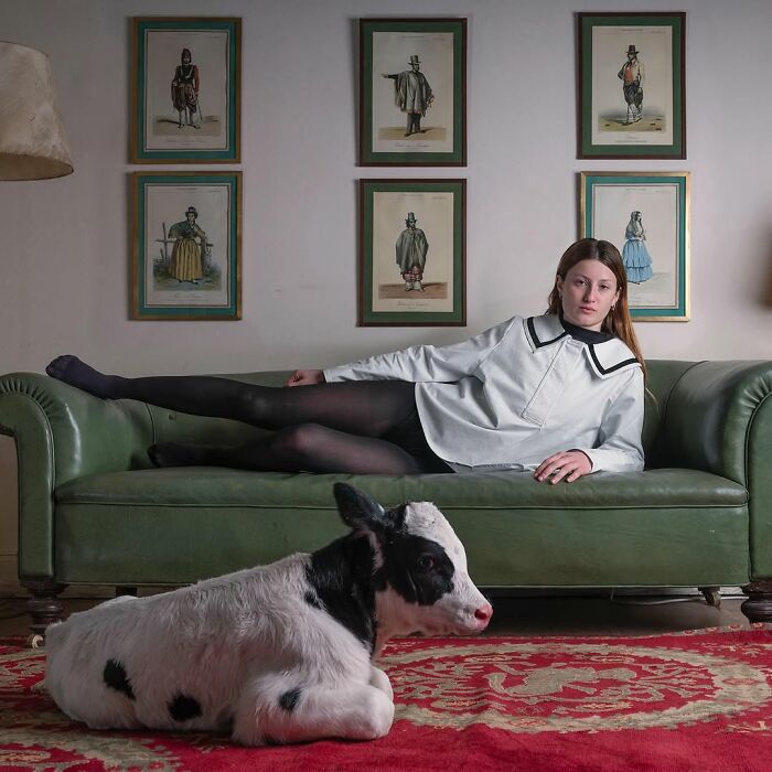Young woman in black and white outfit lies on green sofa next to a black and white calf, pets and their humans look alike.