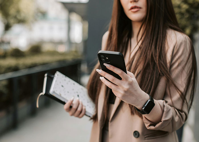 Woman holding phone and notebook outdoors, sharing useful life hacks with others in a casual urban setting