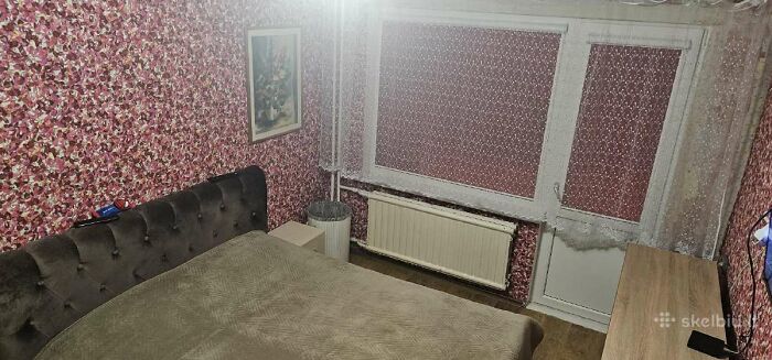 Small bedroom with floral wallpaper, dark upholstered bed, and window with lace curtains in a wild real estate listing.