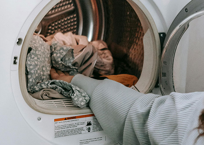 Hand reaching into a dryer filled with clothes, illustrating genius cleaning hacks inspired by laziness and efficiency.
