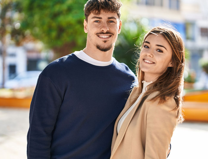 Young woman and man smiling outdoors, representing women sharing important girl code rules in a friendly setting.