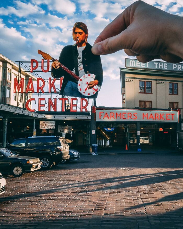 Hand holding a paper cutout of a musician with a clock, creatively interacting with real life at a farmers market.