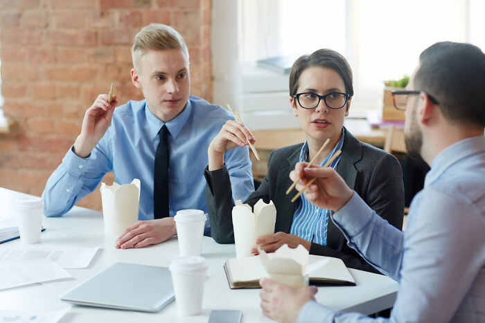 Three workers share unprofessional things done while eating lunch with chopsticks in a casual office meeting.