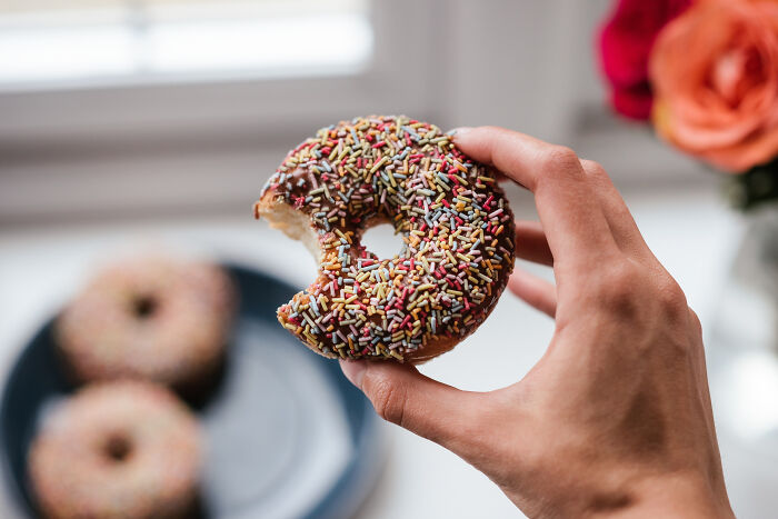 Hand holding a chocolate sprinkled donut, illustrating lovable clueless dads' quirky moments during pregnancy.