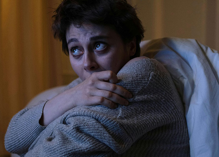 Person in dimly lit room looking scared and hugging themselves after seeing terrifying things found online.