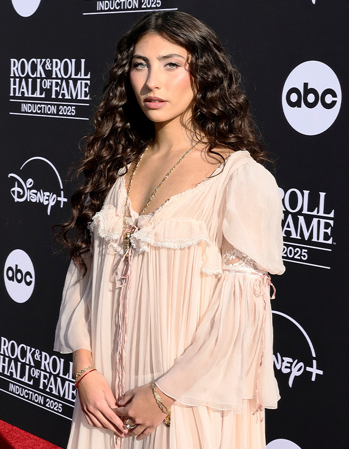 Chappell Roan posing on red carpet at Rock Hall of Fame 2025 event in flowing light pink dress and curly hair.