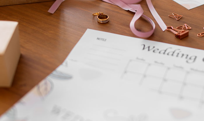 Wedding planner with rings and pink ribbons on wooden table symbolizing bride wants to upgrade honeymoon at bridesmaid&rsquo;s expense.