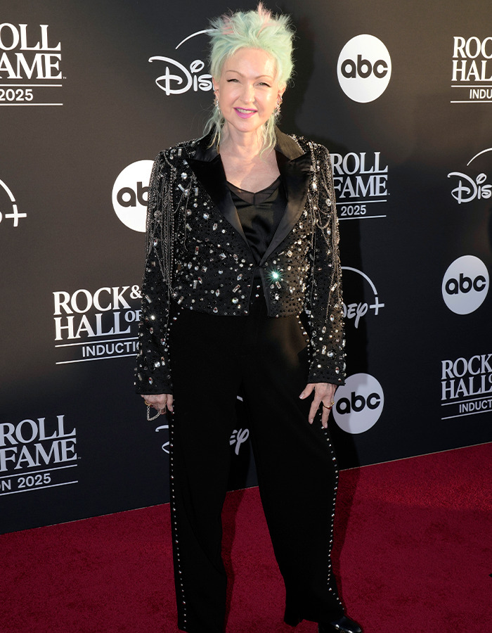 Person with light green hair in a studded black jacket and pants posing on the Rock Hall of Fame 2025 red carpet.