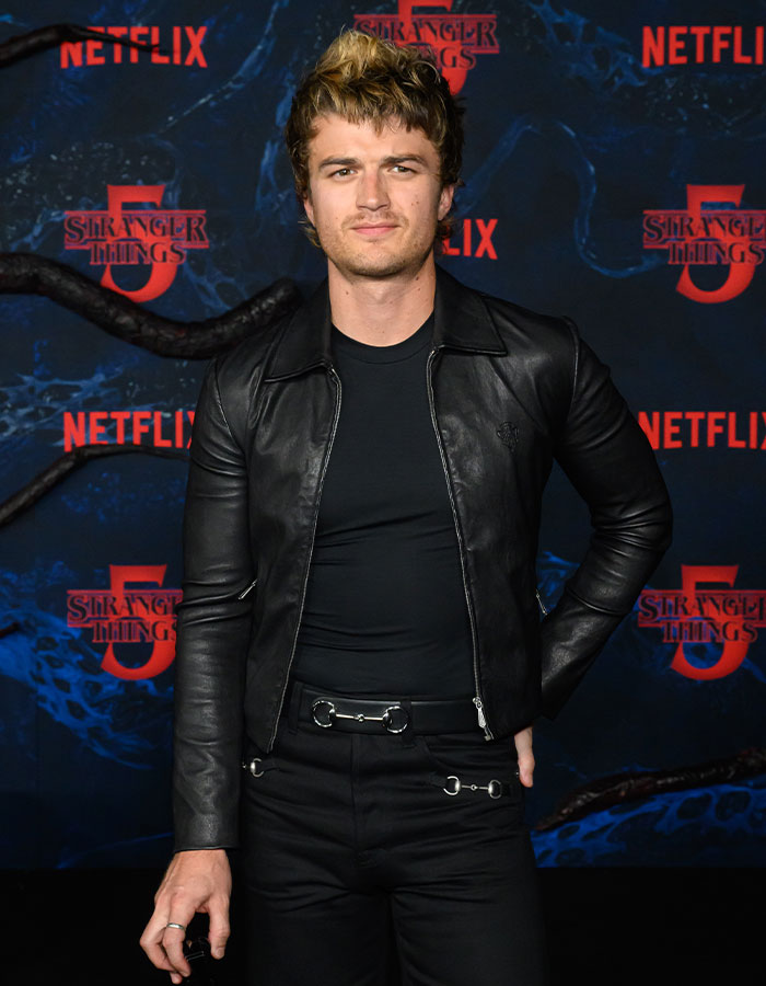 Actor wearing a black leather jacket and pants with silver details at the Stranger Things 5 premiere red carpet event.