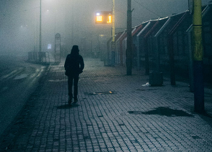 A solitary figure walking on an empty, foggy street at night, evoking bizarre events that creep people out.