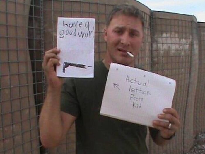 U.S. soldier holding letters kids send, one with a drawing of a gun and the message have a good war