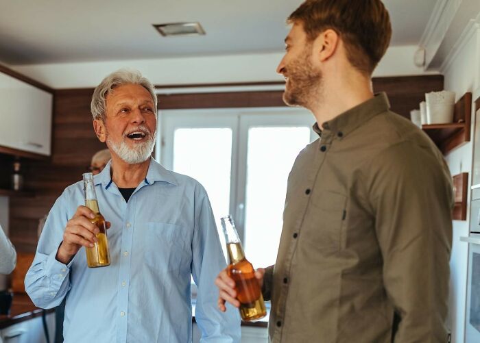 Two men, representing clueless dads, smiling and holding bottles in a kitchen during a casual moment.