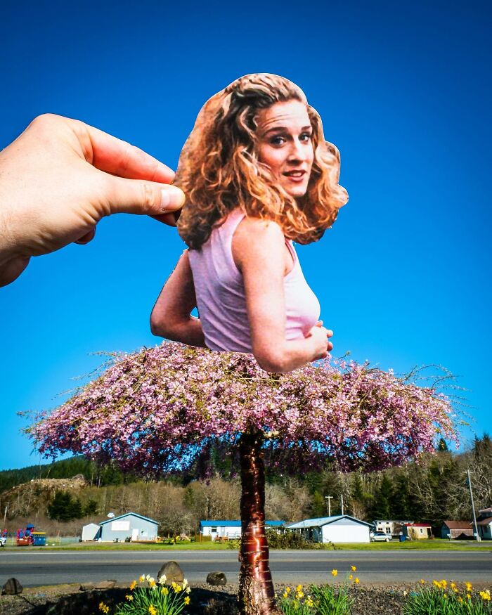 Hand holding a paper cutout of a woman cleverly aligned with a tree, showcasing brilliant paper cutouts by Rudy Willingham.