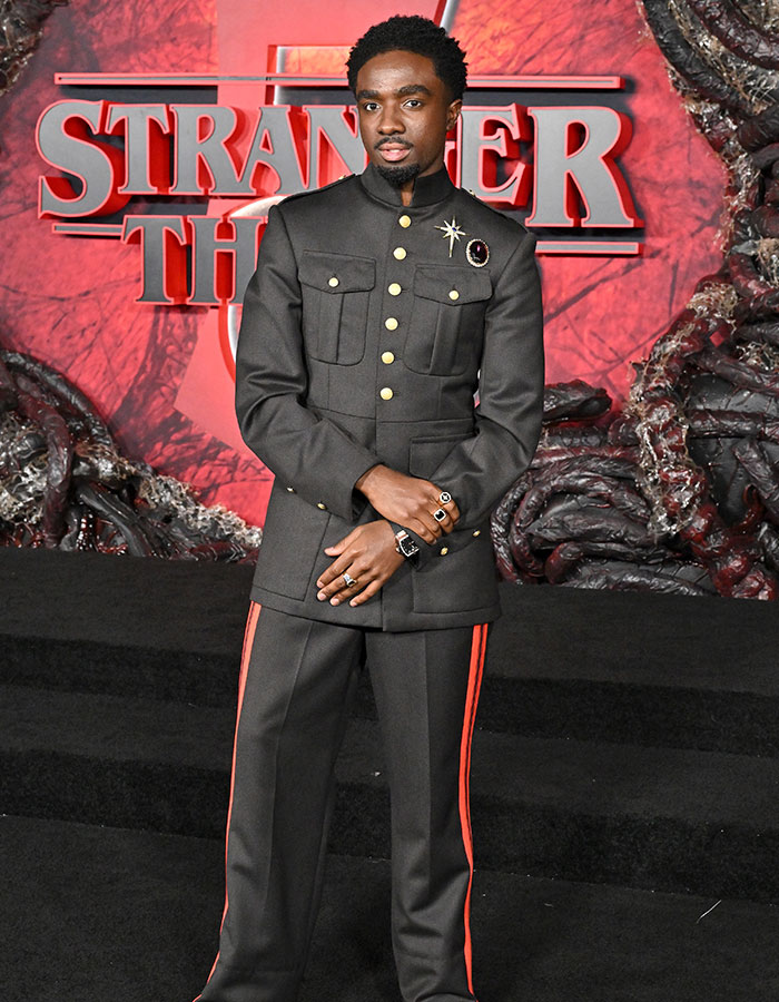 Actor in a unique military-style outfit with gold buttons and red stripes at Stranger Things 5 red carpet premiere.