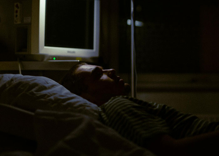 Person lying in a dark room with a monitor nearby, evoking creepy and bizarre events atmosphere