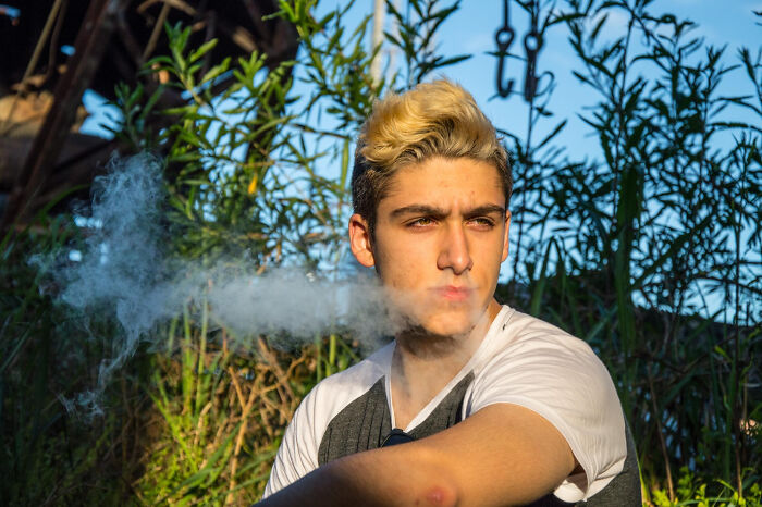 Young man outdoors exhaling smoke thoughtfully, illustrating stories of compulsory things in life being optional.