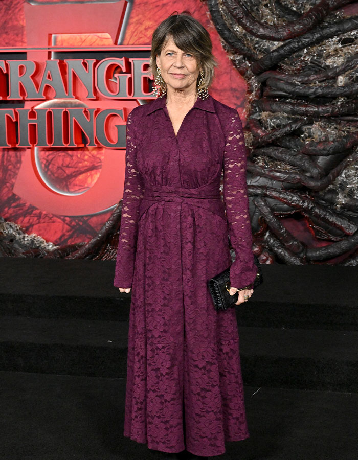 Woman in a long-sleeve purple lace dress posing at a red carpet event for Stranger Things 5 premiere.