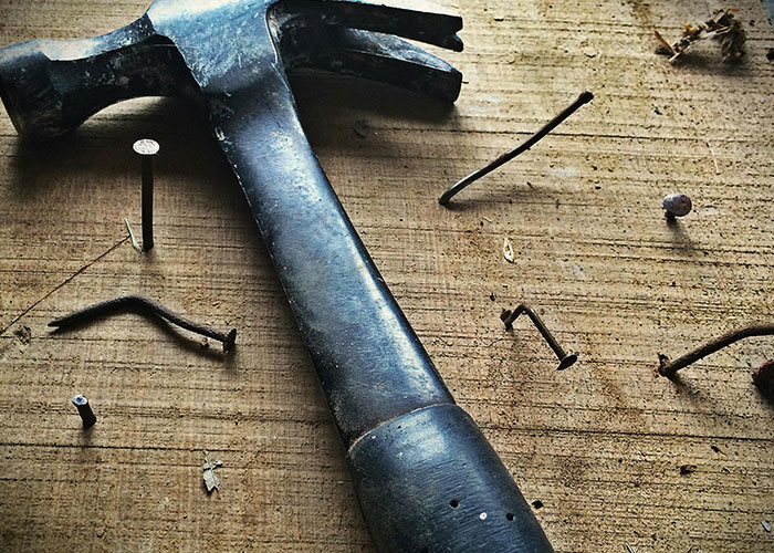 Old claw hammer surrounded by rusty nails found inside the walls of a home during renovations and repairs.