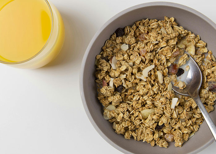 Bowl of granola with a spoon next to a glass of orange juice, illustrating simple life hacks for easy mornings.