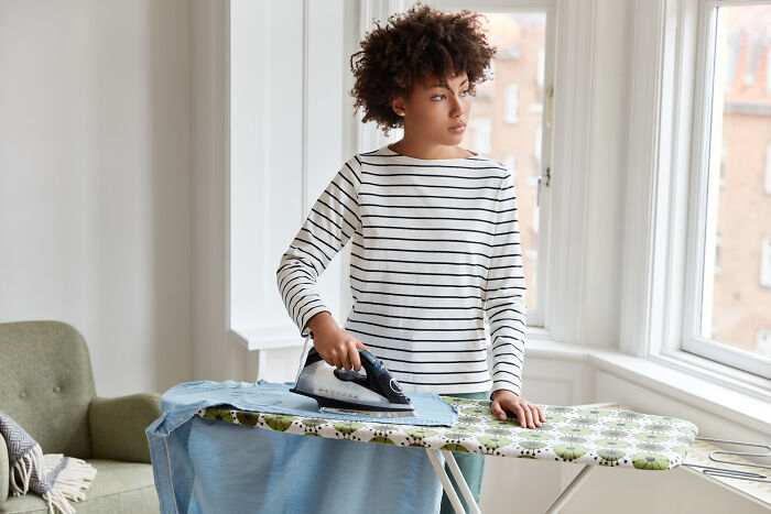 Woman ironing clothes by a window, symbolizing stories of realizing compulsory life tasks are actually optional.