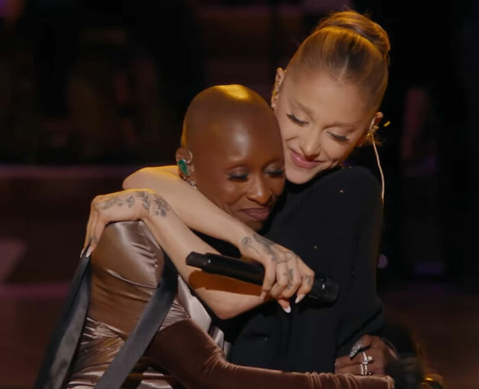 Cynthia Erivo and Ariana Grande sharing a warm hug during a live performance, showcasing their unique interaction.