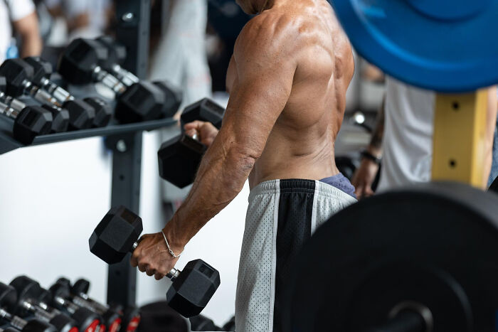 Muscular man lifting dumbbells at the gym, showing strength and focus in a workout setting.