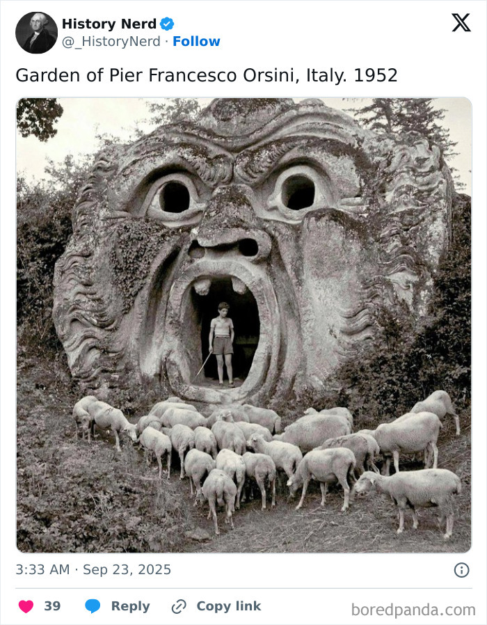 Black and white photo showing a person and sheep at a giant stone face sculpture in an Italian garden, exploring history.