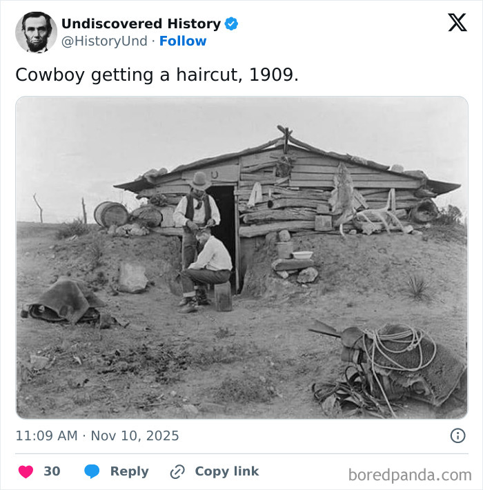 Cowboy in 1909 getting a haircut outside a rustic log cabin in a fascinating photo revealing a moment lost to time